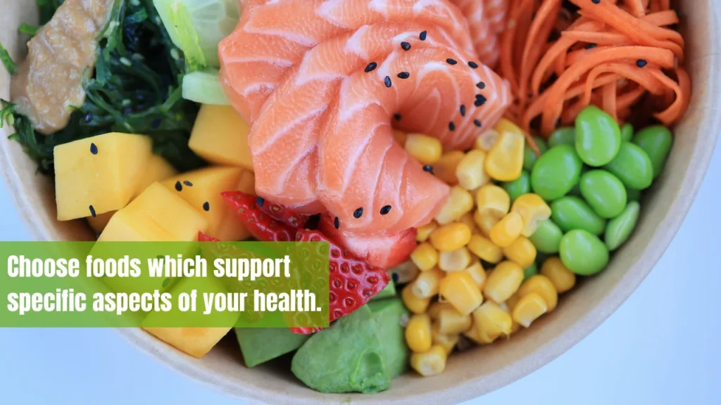 A colorful bowl with salmon, edamame, corn, carrots, mango, strawberries, avocado, and leafy greens.